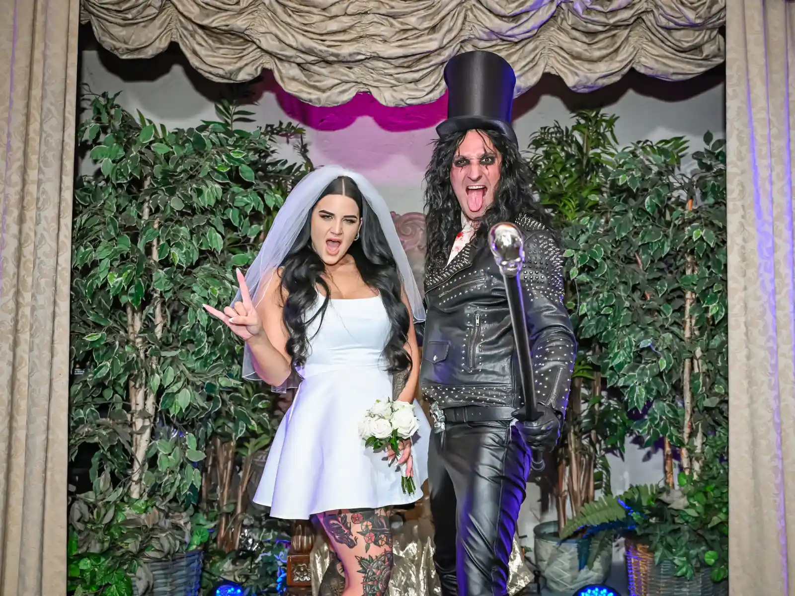 A bride posing with an Alice Cooper impersonator, both making rock-and-roll hand gestures.