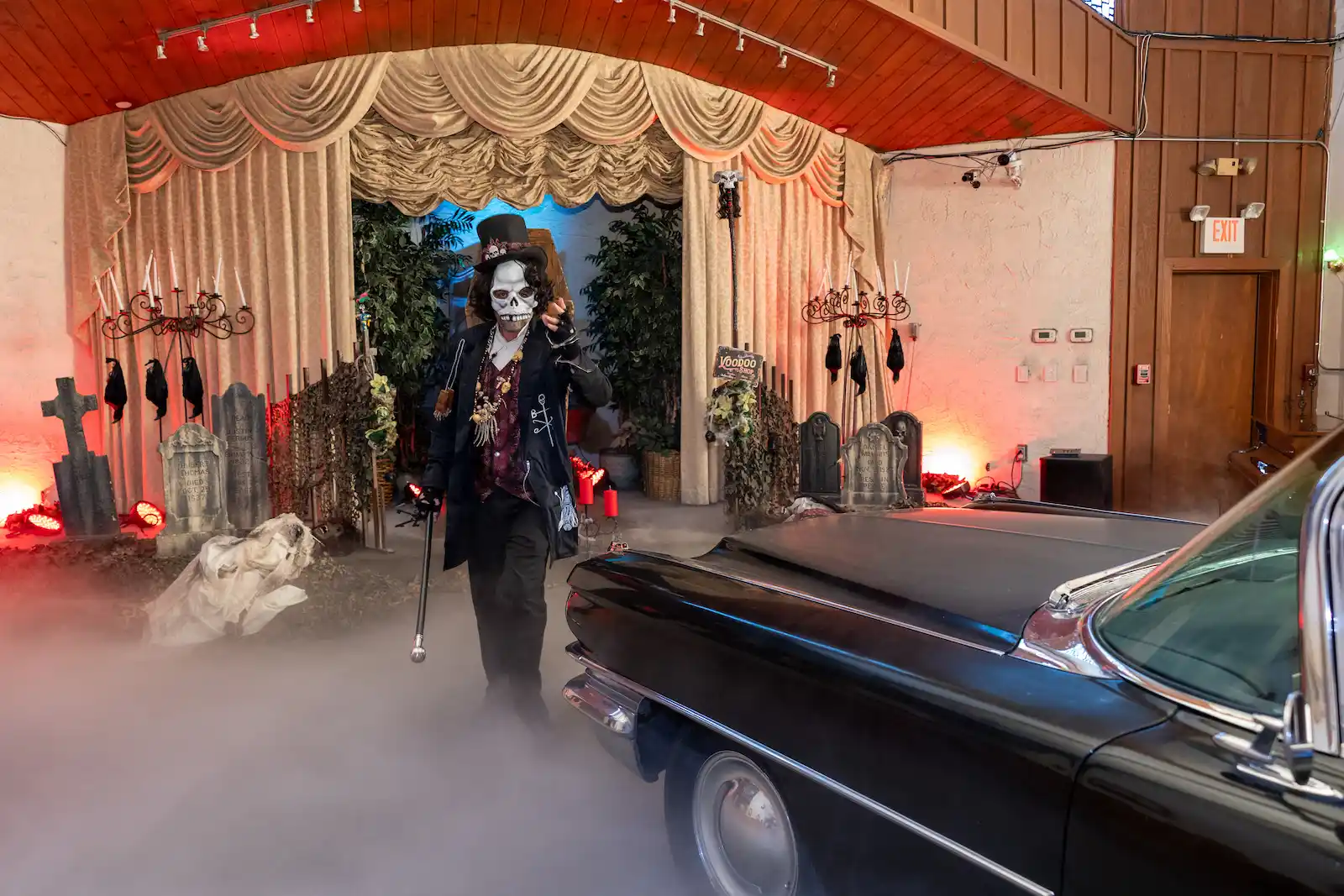 Voodoo skeleton impersonator with top hat and cane walking beside black cursed hearse through graveyard stage fog at Las Vegas themed wedding