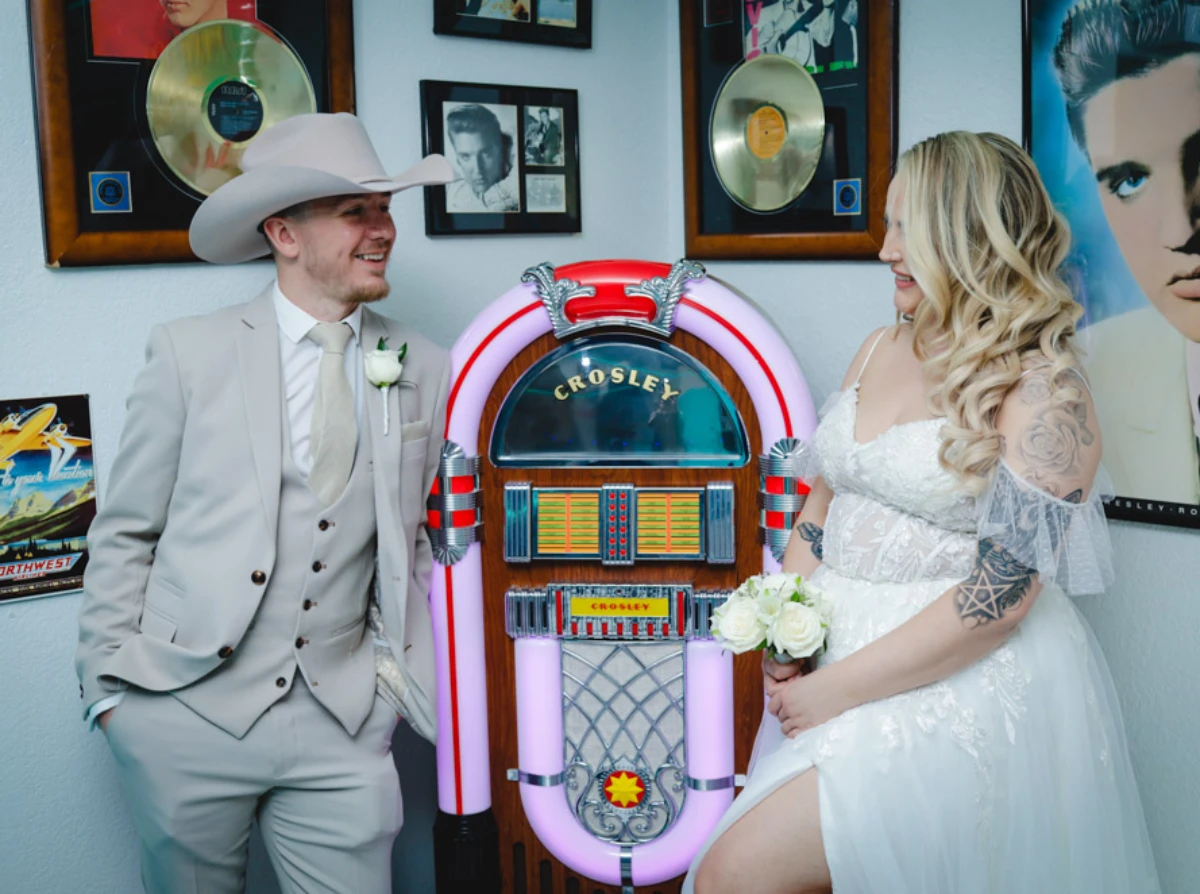 Vintage Las Vegas wedding couple posing beside retro jukebox in rock-and-roll themed chapel surrounded by classic Elvis memorabilia