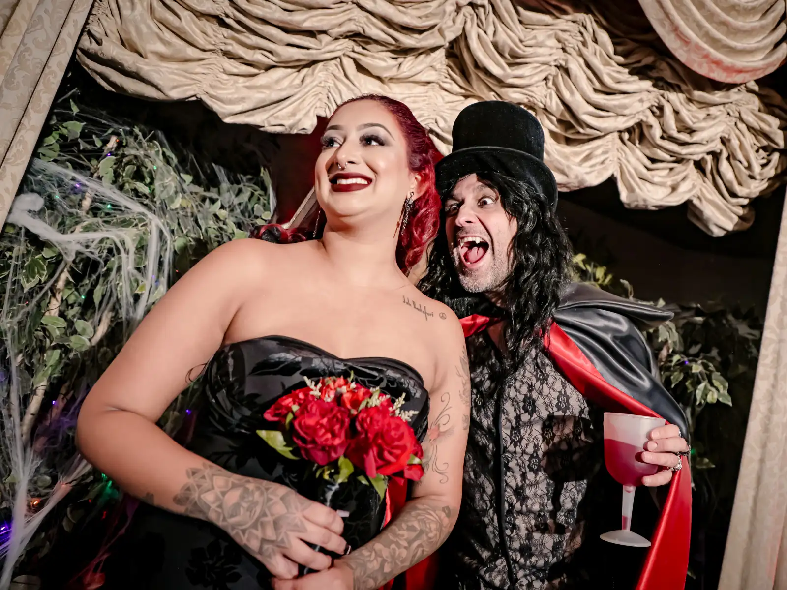 Bride in black dress with red roses laughing with Dracula impersonator in top hat and red cape at Viva Las Vegas vampire themed wedding