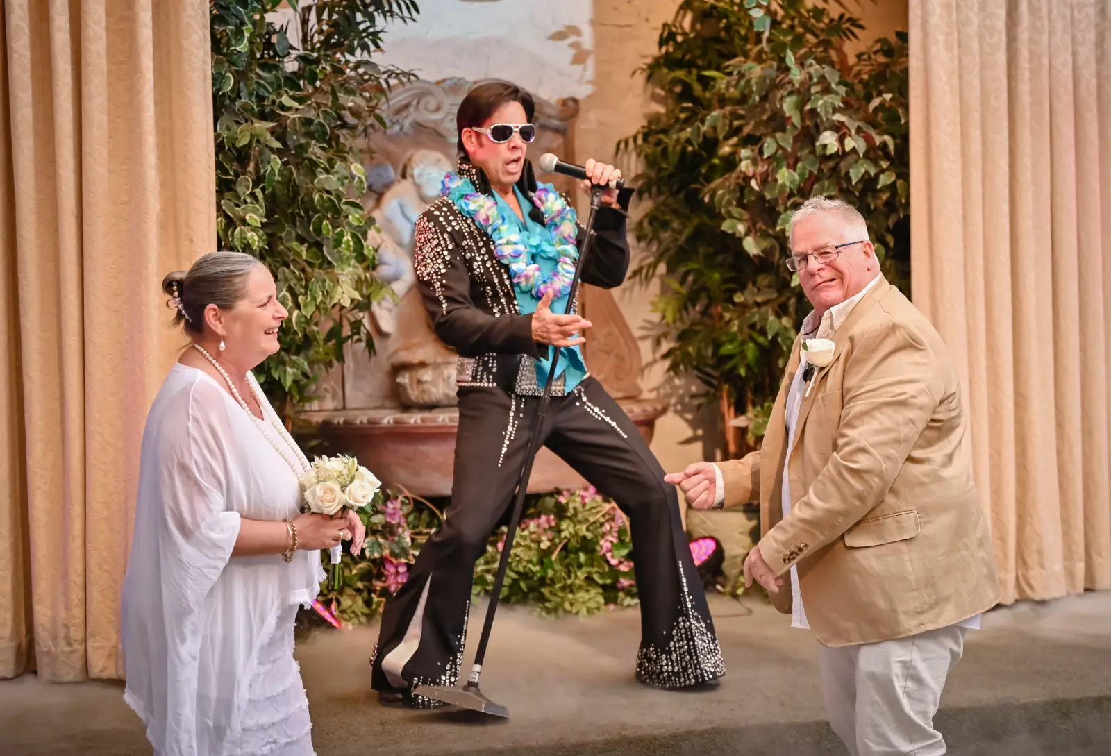 Elvis impersonator singing during fun wedding ceremony while smiling couple holds bouquet on chapel stage