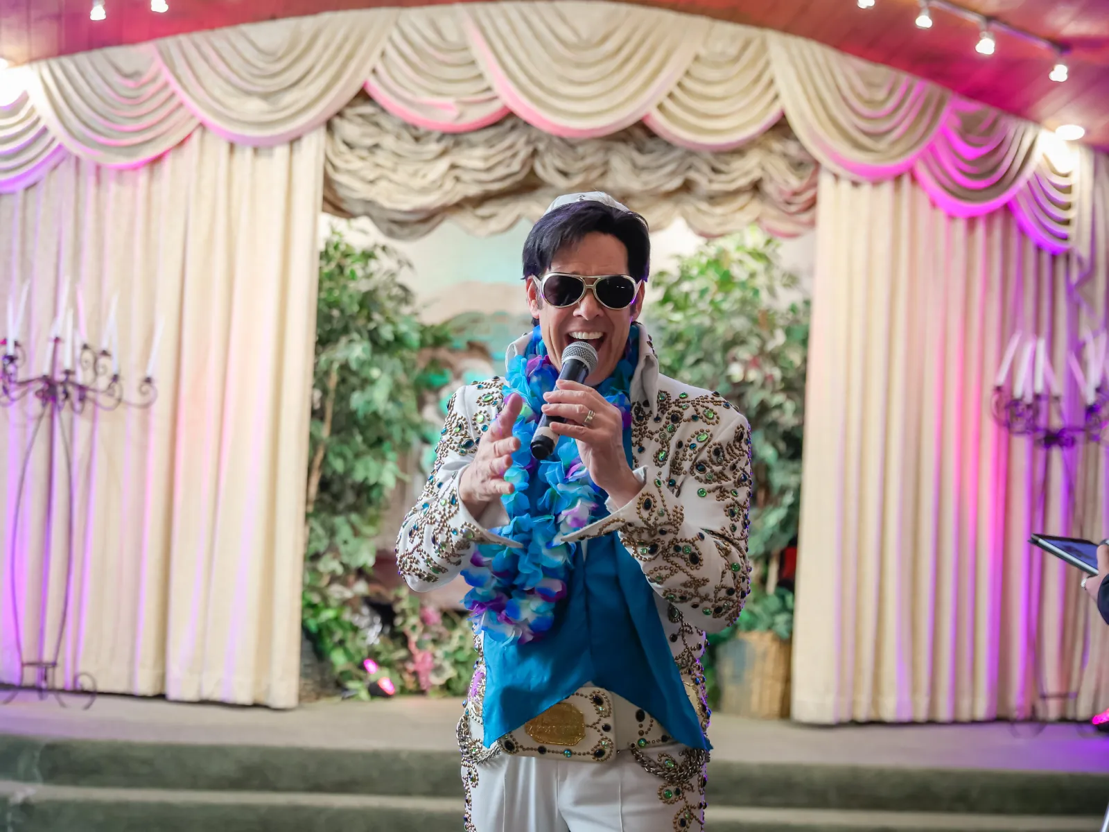 Elvis impersonator singing into microphone on chapel stage during lively themed wedding ceremony