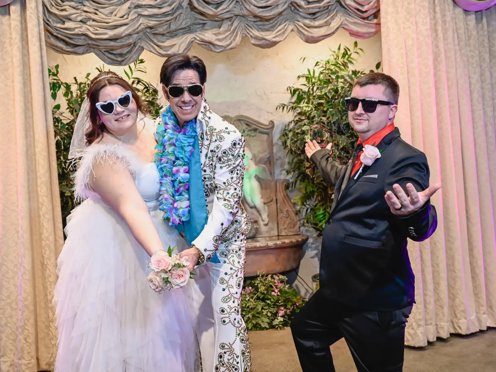 Elvis impersonator posing playfully with bride and groom wearing sunglasses during fun chapel wedding photo