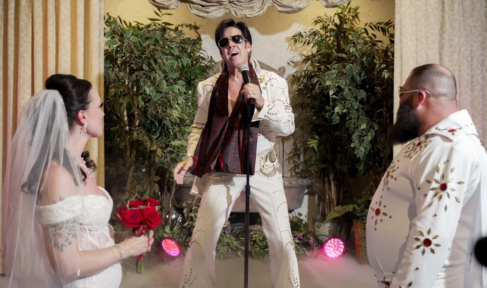 Las Vegas Elvis wedding ceremony with bride holding red roses and groom watching Elvis impersonator sing in chapel