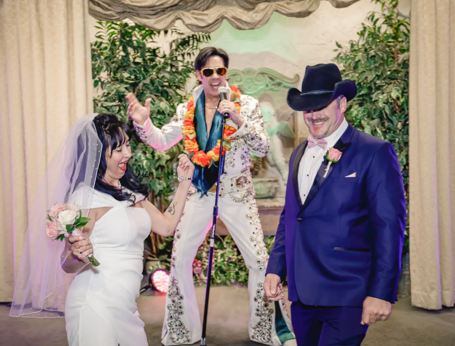 Fun Las Vegas Elvis wedding ceremony with bride dancing and groom in cowboy hat smiling on chapel stage