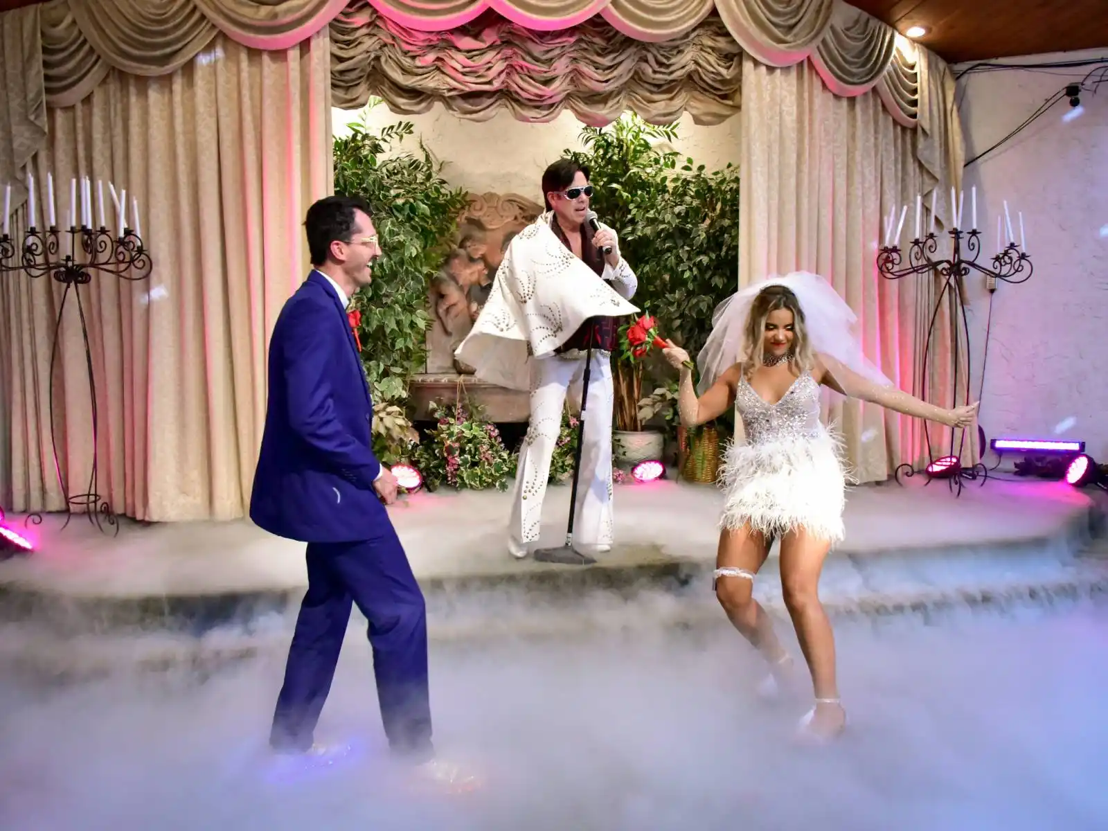 Bride and groom dancing with Elvis impersonator singing on stage with fog effects at a Las Vegas wedding chapel ceremony
