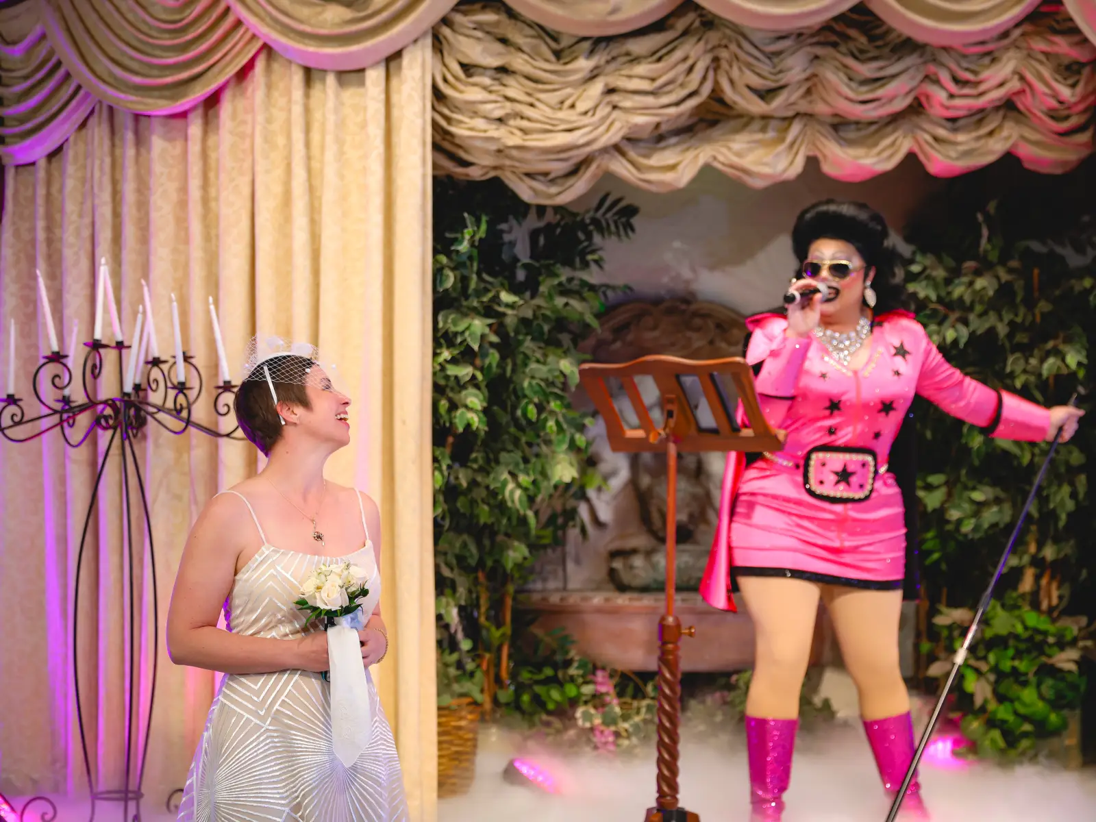 Elvis-style officiant in pink outfit singing during wedding ceremony while bride smiles at altar.