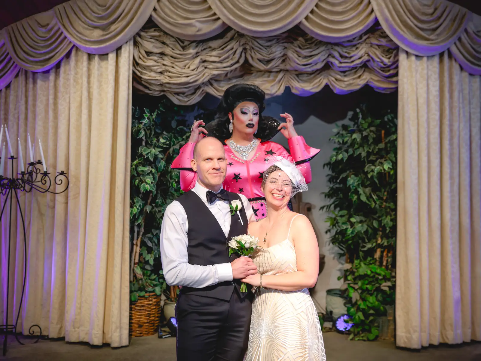 Newlywed couple posing at altar with Elvis-style officiant in pink outfit behind them.