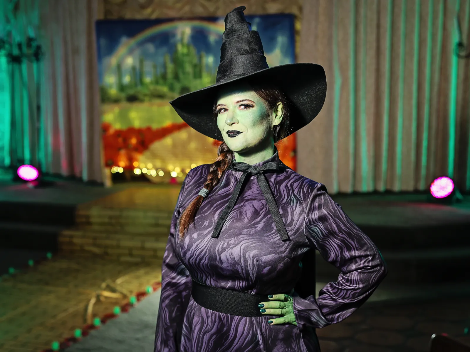 Wicked Witch impersonator with green makeup and black hat in front of Emerald City backdrop at a Las Vegas wedding chapel