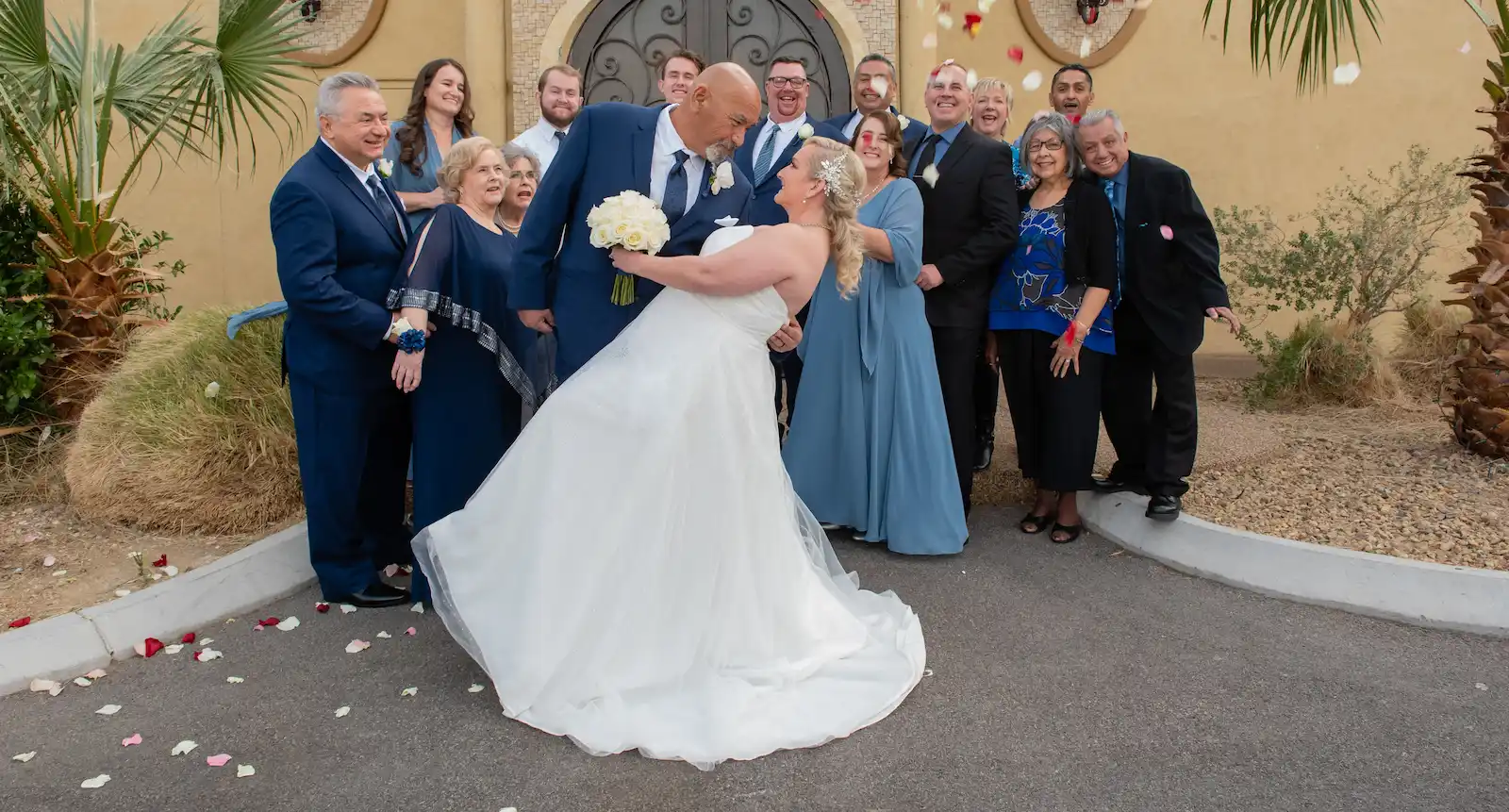 Newlyweds dipping outside Las Vegas wedding chapel entrance with family and rose petals
