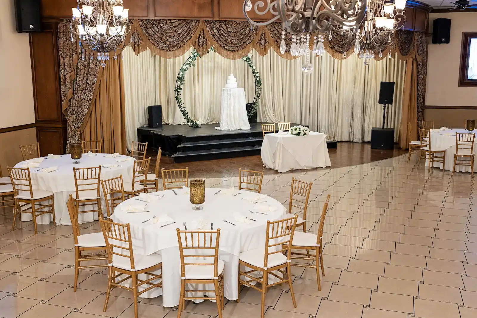 Elegant wedding reception hall with white tablecloths, gold chiavari chairs and floral arch at the Viva Las Vegas Event Center.