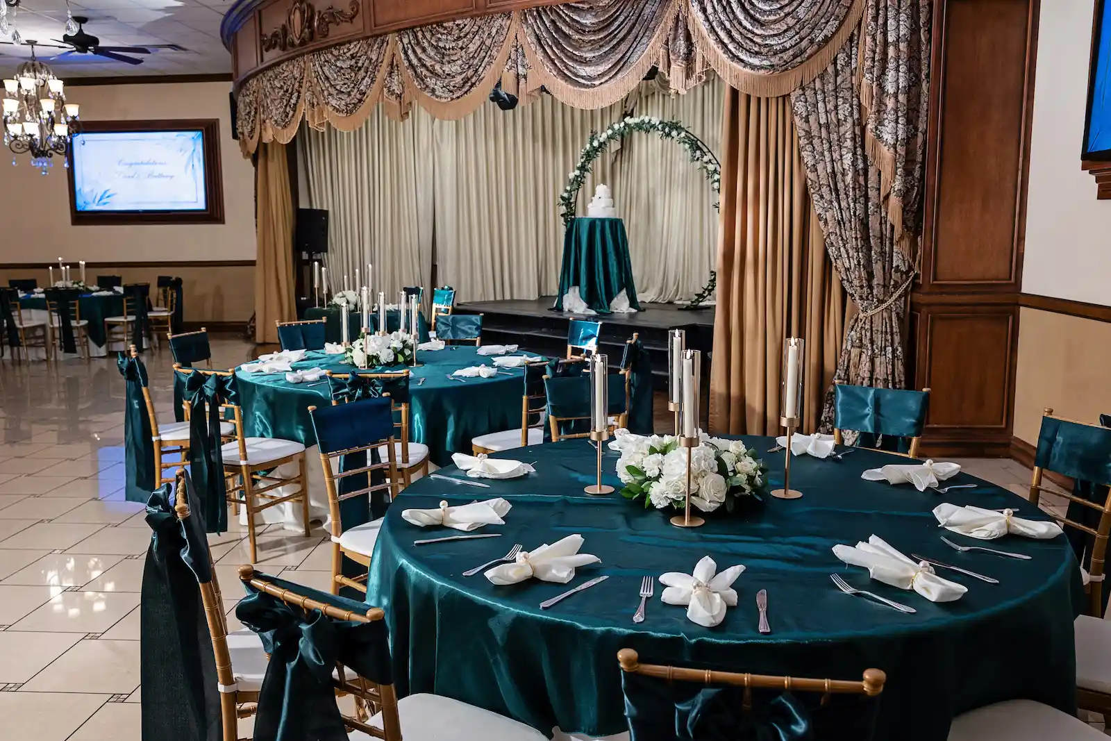 Viva Las Vegas Event Center banquet hall set with teal velvet tablecloths, gold chiavari chairs, white roses and candle centerpieces.