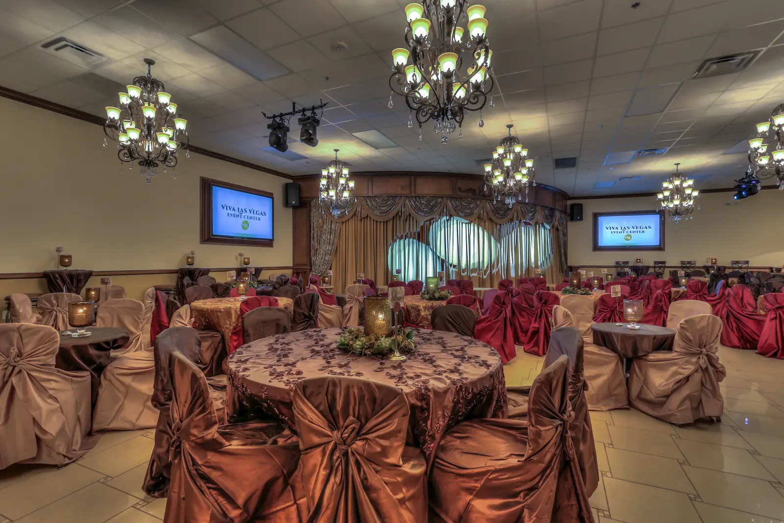 Viva Las Vegas Event Center banquet hall with burgundy and gold chair covers, chandeliers, and stage