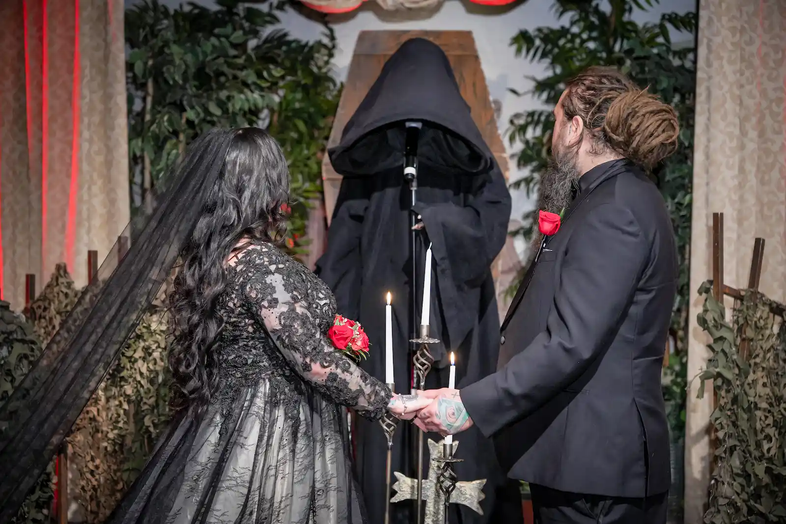 Bride in a black lace gown and groom holding hands before a Grim Reaper officiant at a Las Vegas gothic wedding.