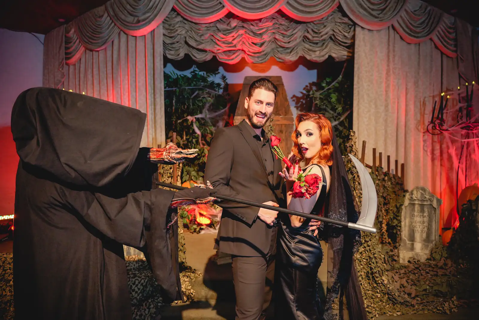 Smiling couple posing with a Grim Reaper holding a scythe at a Las Vegas halloween graveyard wedding venue.