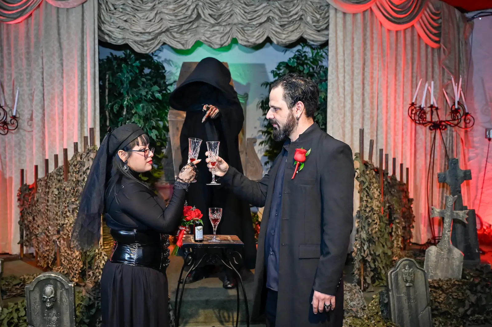 Couple lighting candles together during a gothic Las Vegas wedding ceremony with a Grim Reaper officiant behind them