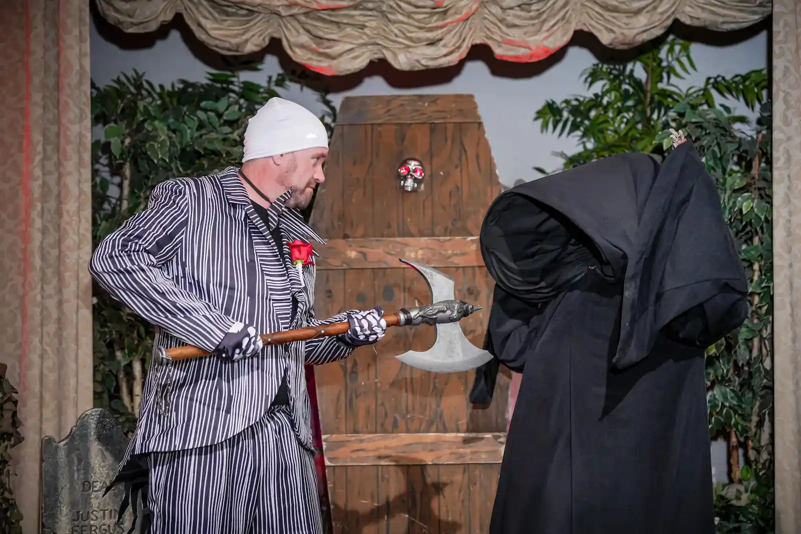 Groom in a striped suit holding an axe in a standoff with a Grim Reaper in front of a coffin at a Las Vegas wedding.
