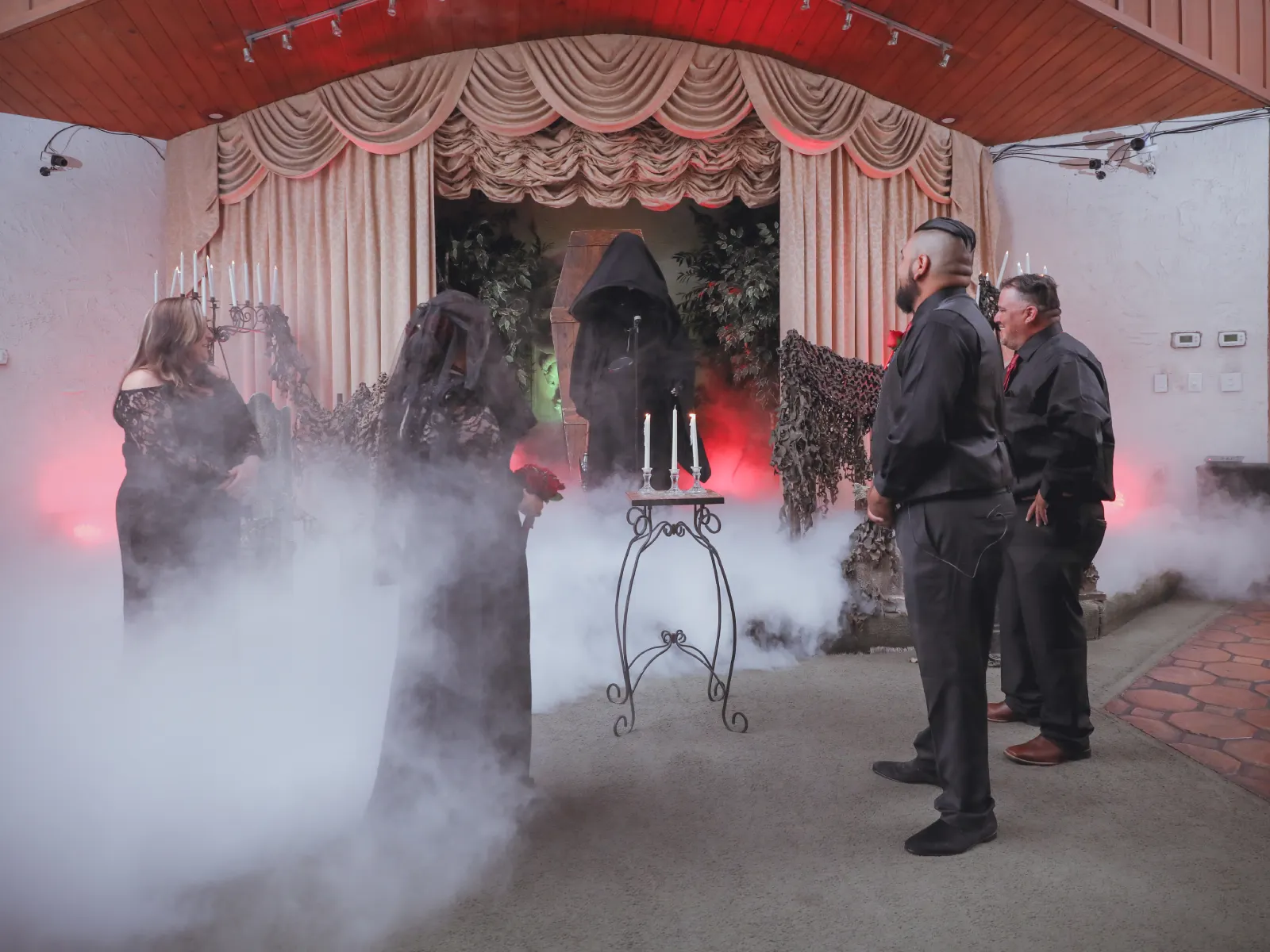 Grim reaper officiant emerging from coffin surrounded by stage fog with bride and groomsmen at Viva Las Vegas horror themed wedding ceremony