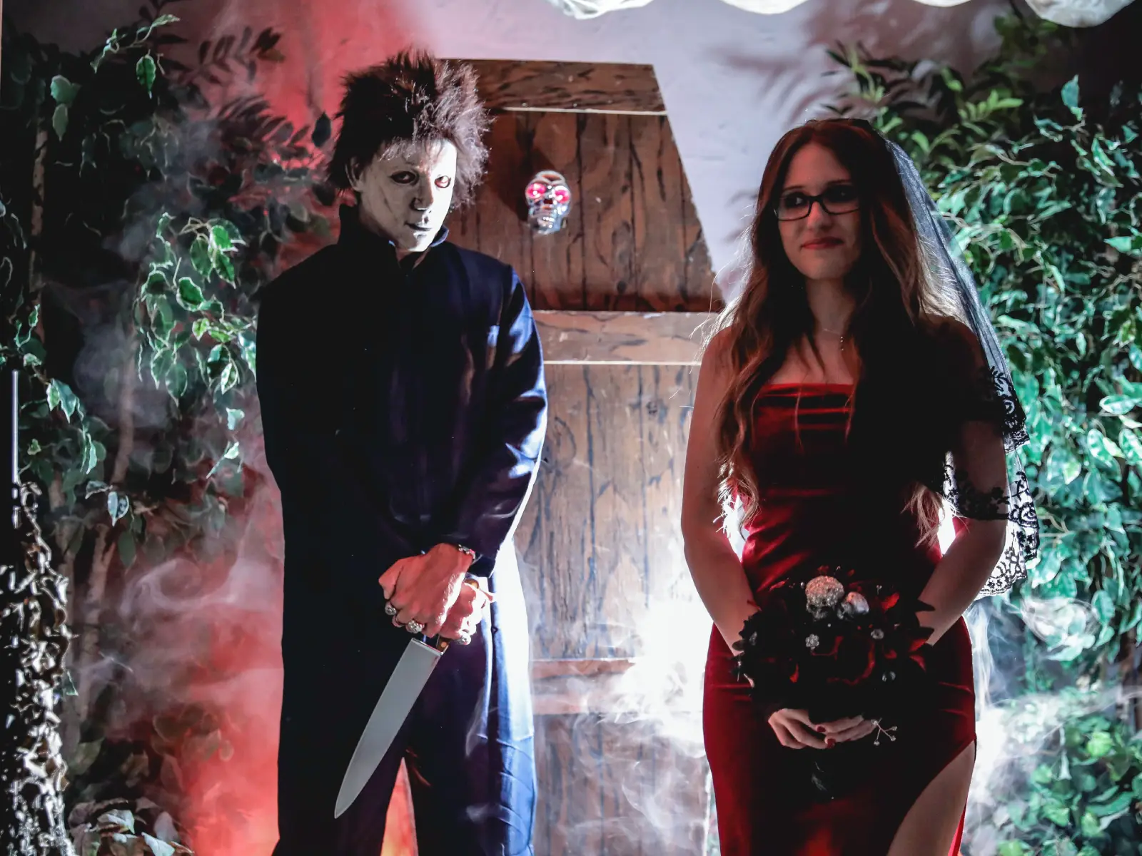 Michael Myers impersonator escorting bride in black veil and red dress through fog at Las Vegas themed wedding chapel