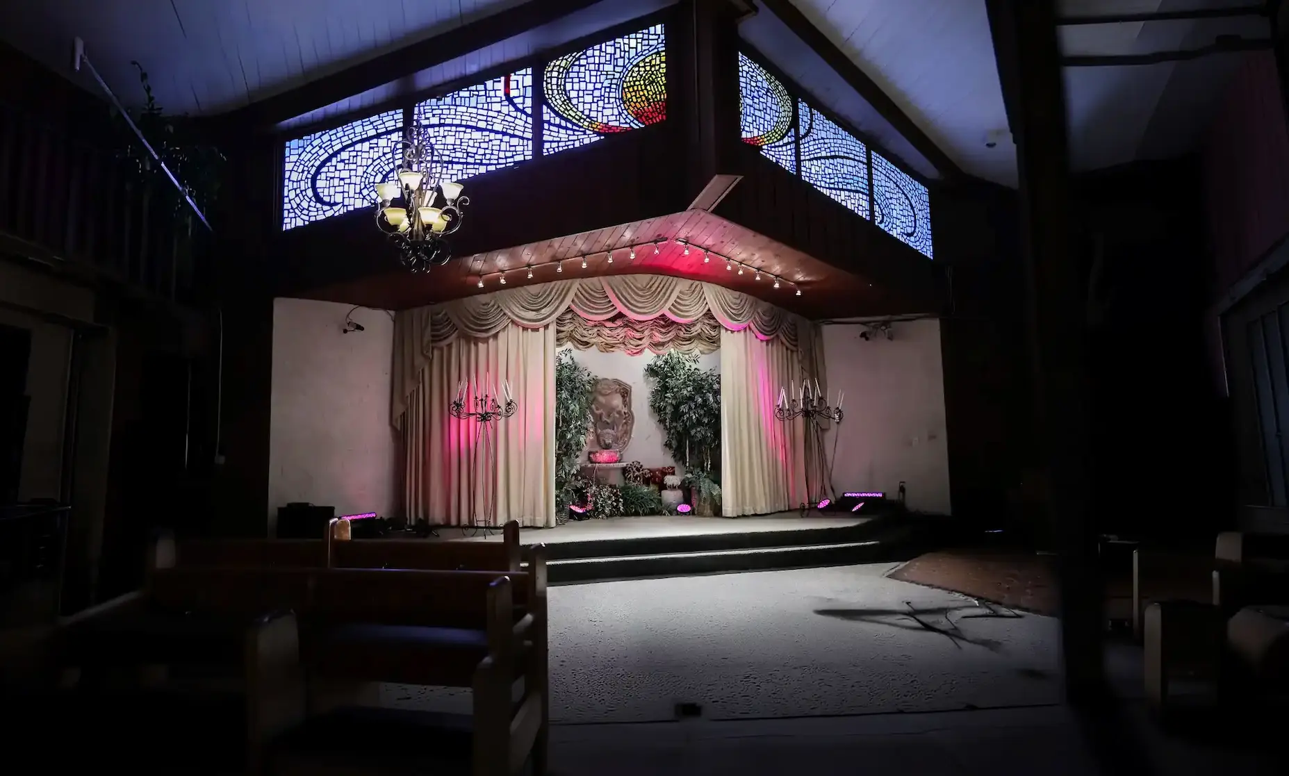 Wide view of Las Vegas wedding chapel interior with stained glass windows, chandelier, and couple kissing on stage