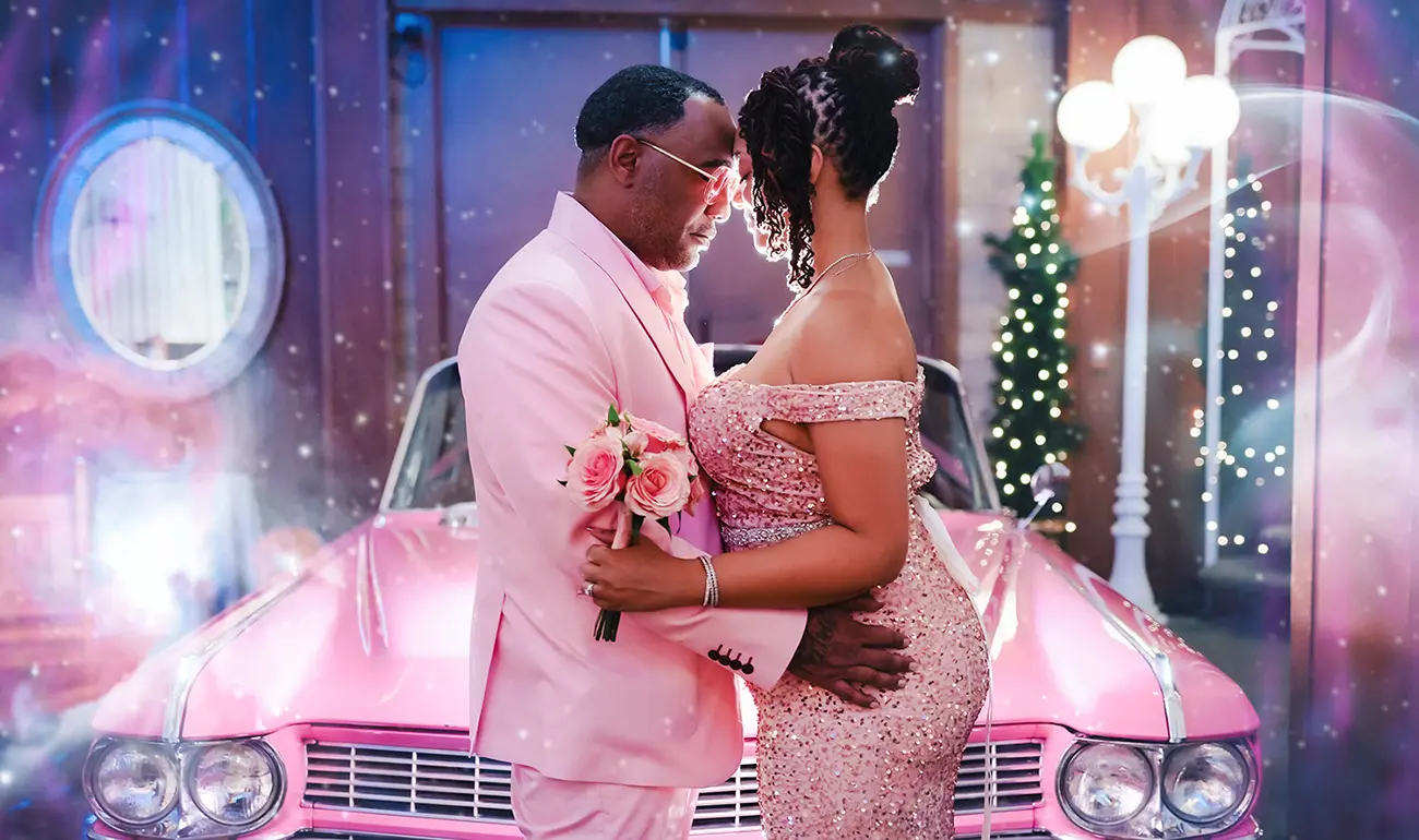 Couple in matching pink embracing in front of pink Cadillac with string lights at Las Vegas wedding chapel