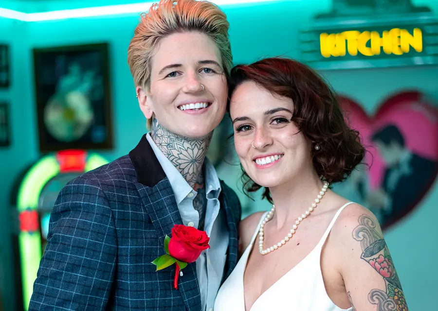 Smiling LGBTQ couple with red rose boutonniere in retro diner at Las Vegas chapel