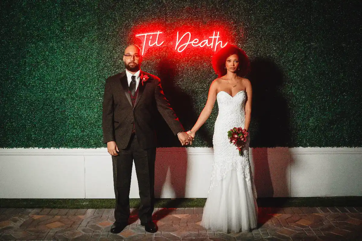 Newlywed couple holding hands under til death neon sign at Las Vegas wedding chapel