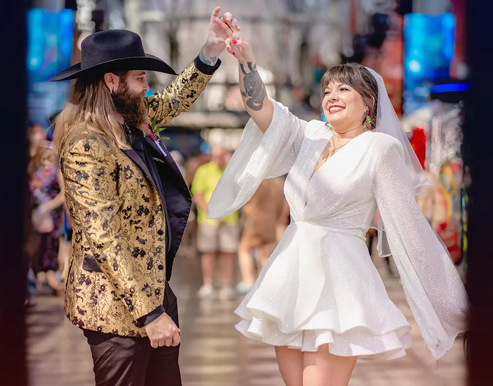 Groom in cowboy hat twirling bride in white dress on Fremont Street in Las Vegas