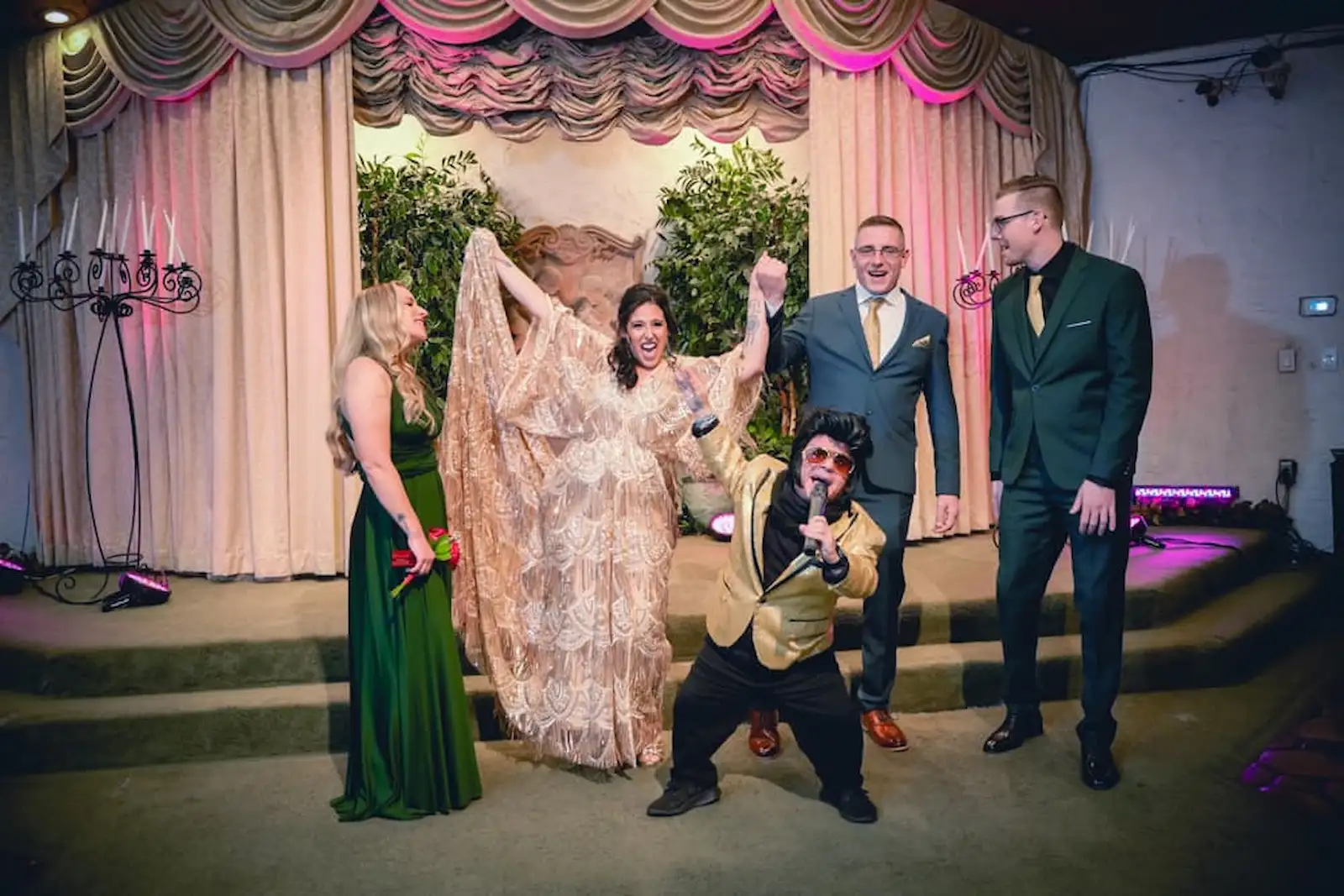 Wedding party celebrating with mini Elvis impersonator in gold jacket performing on stage at a Las Vegas wedding chapel
