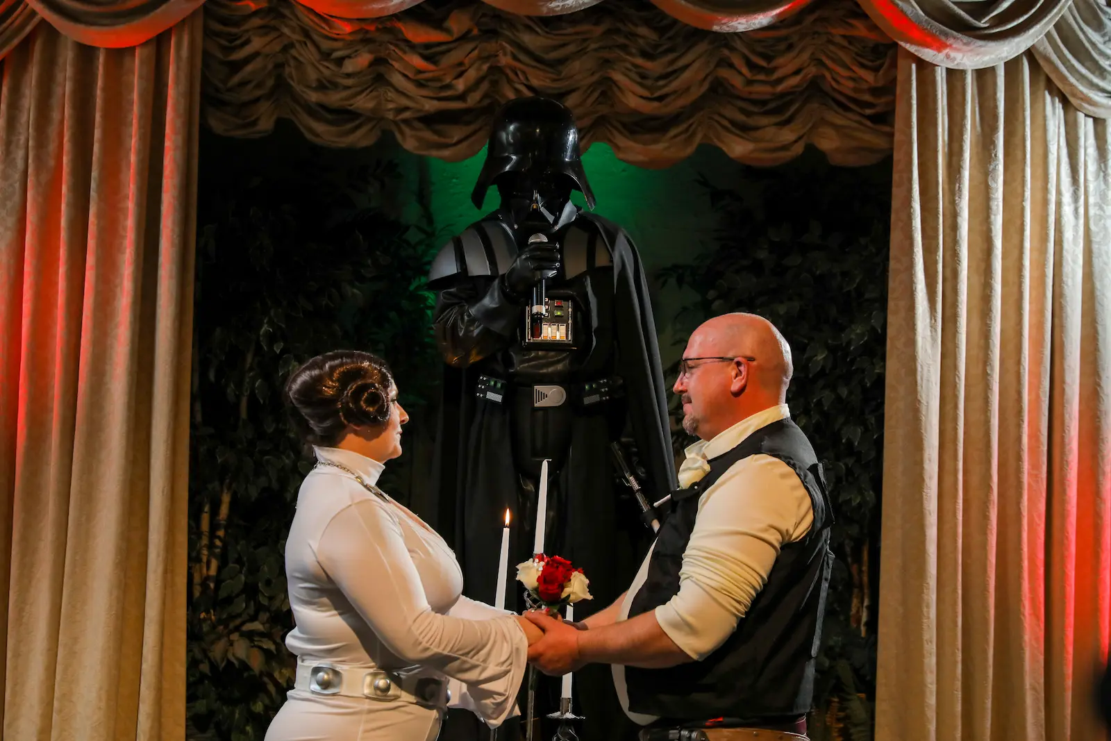 Darth Vader impersonator officiating wedding ceremony as couple in Princess Leia and Han Solo costumes hold hands at Las Vegas chapel