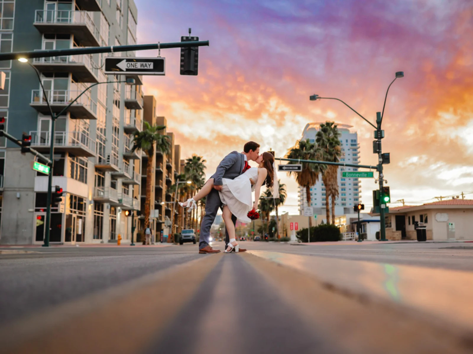 A groom dipping and kissing his bride in the middle of a downtown Las Vegas street during a vibrant orange and purple sunset.