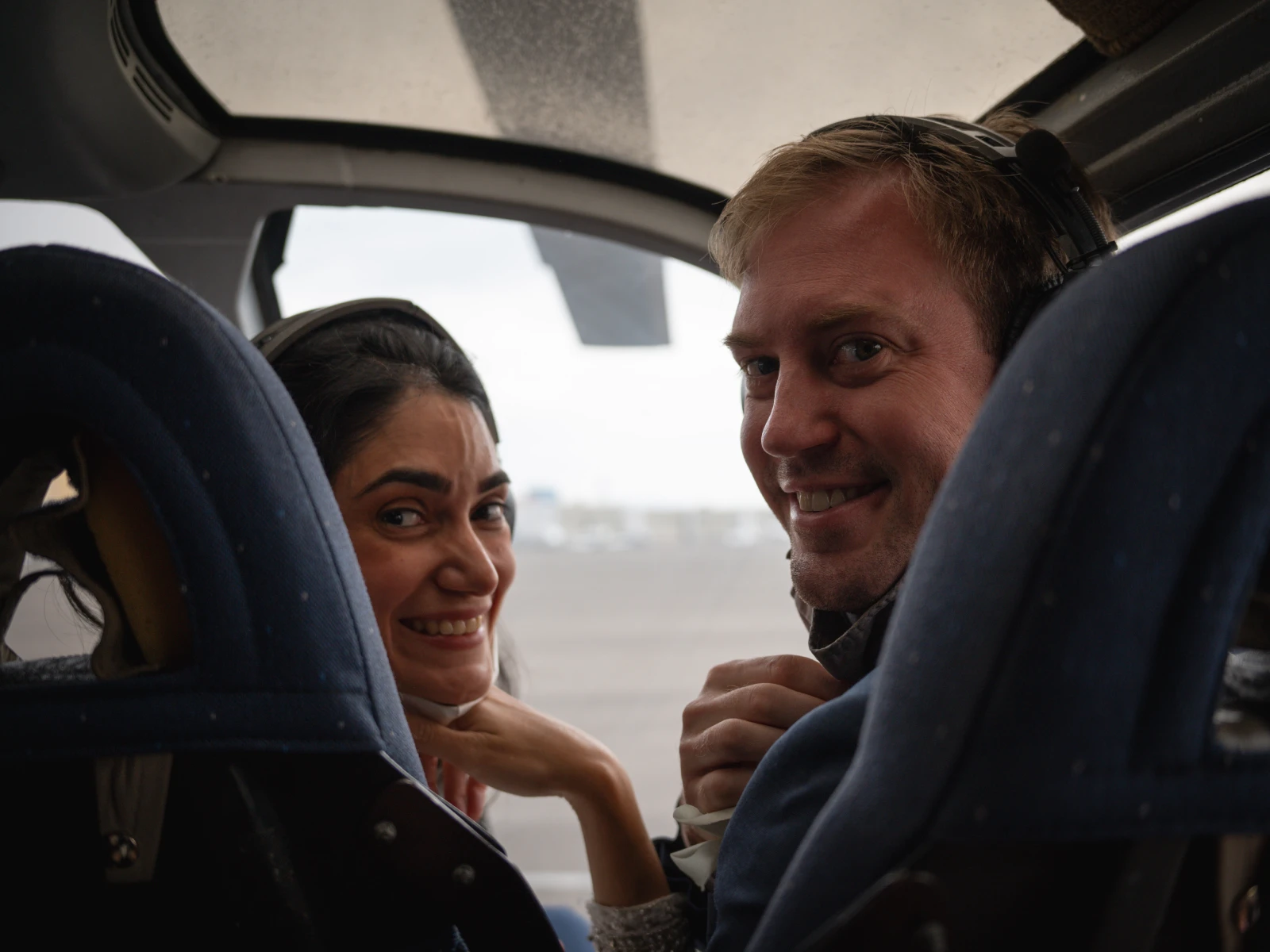 A candid shot of a couple sitting in the cockpit of a helicopter, looking back and smiling at the camera while wearing communication headsets.