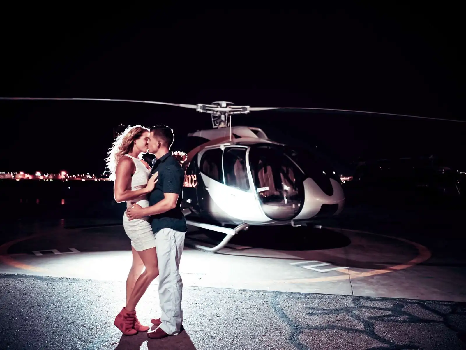 Couple kissing on helicopter landing pad at night with helicopter behind them in Las Vegas