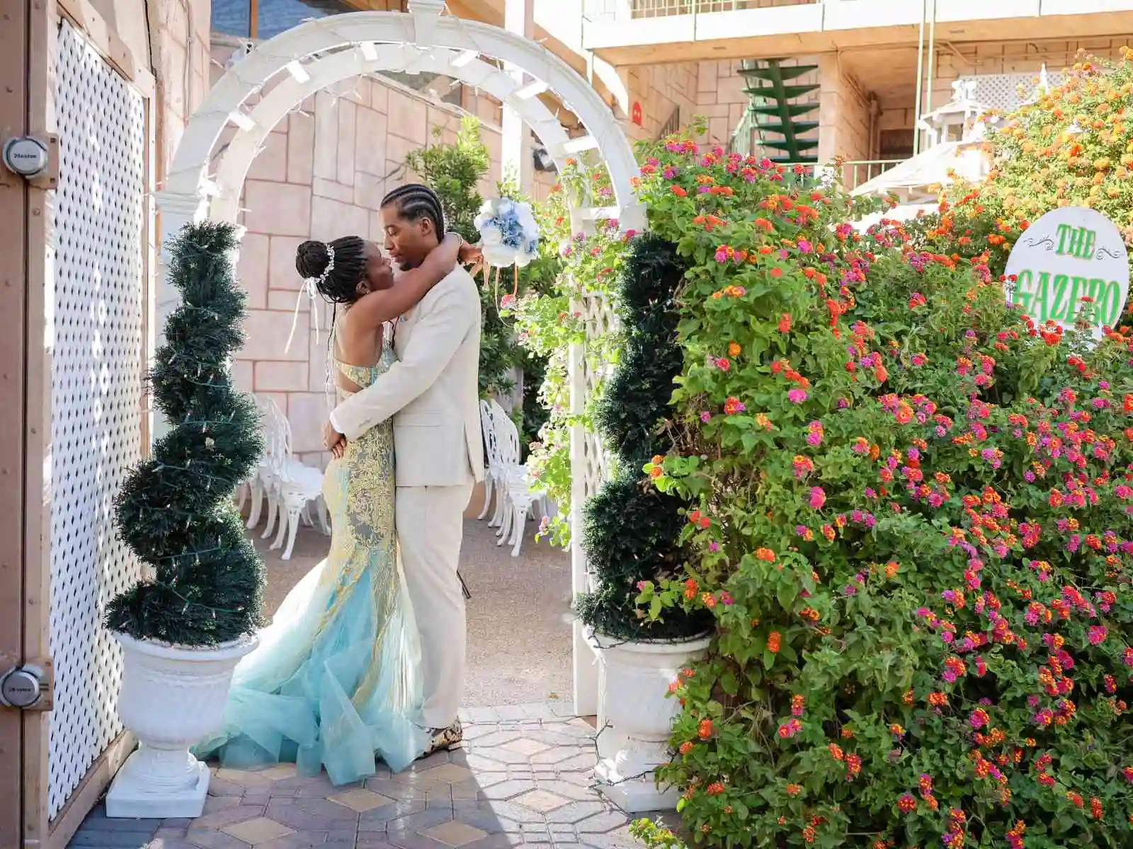 Couple kissing under white garden arch with topiaries and colorful flowers at a Las Vegas wedding chapel gazebo