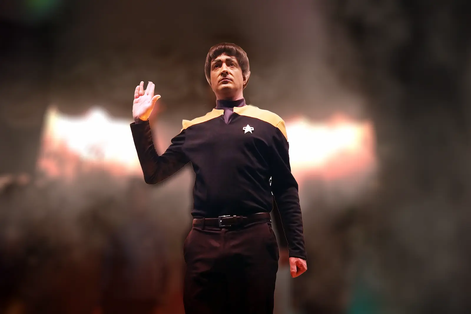 Spock impersonator in Starfleet uniform performing Vulcan salute with dramatic stage fog and lighting