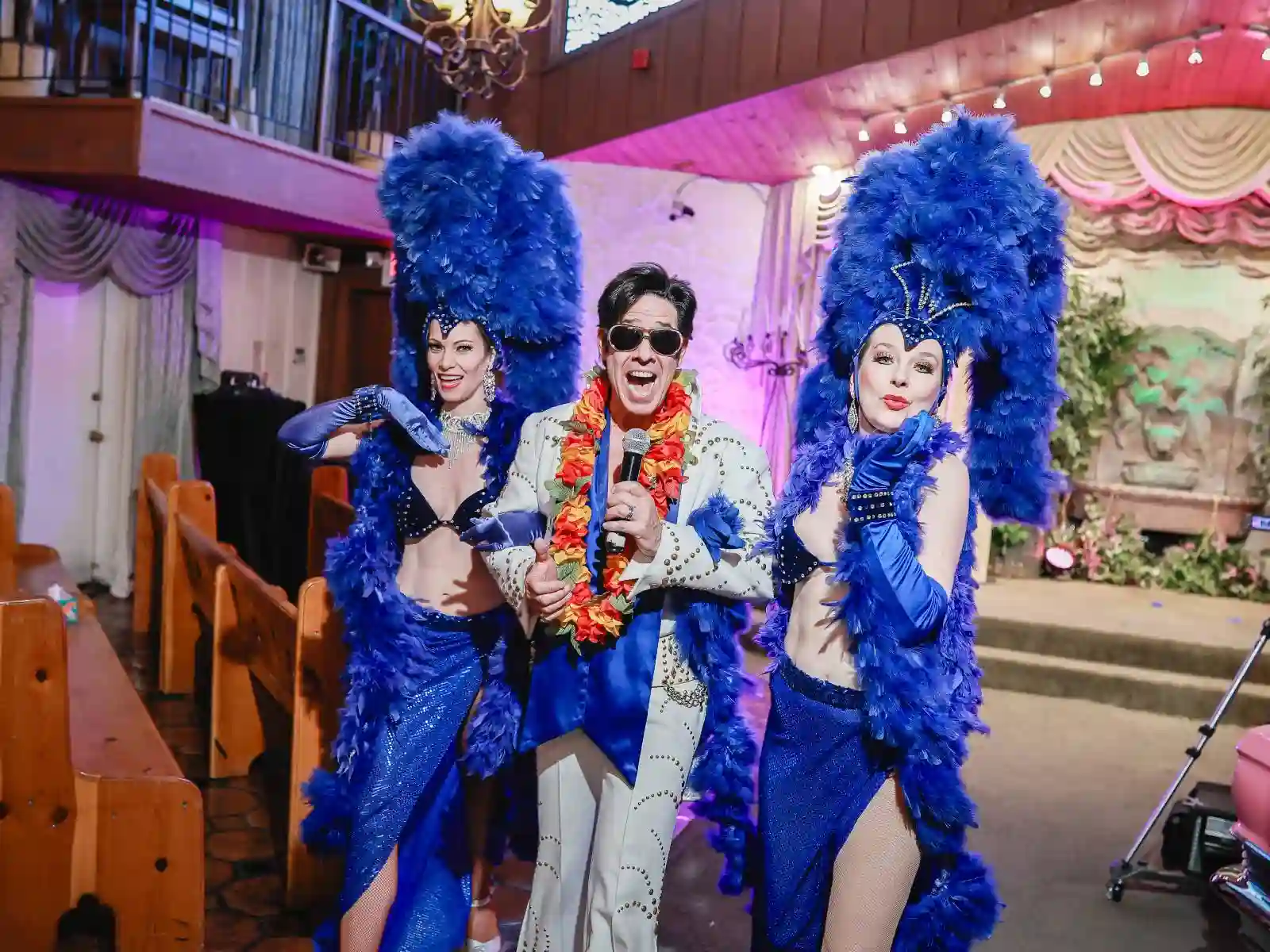 Elvis impersonator with two showgirls in blue feather headdresses performing at a Las Vegas wedding chapel