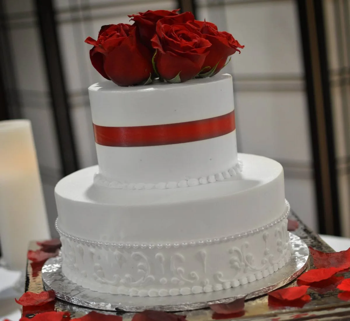 Two-tier white wedding cake topped with red roses and a red satin ribbon