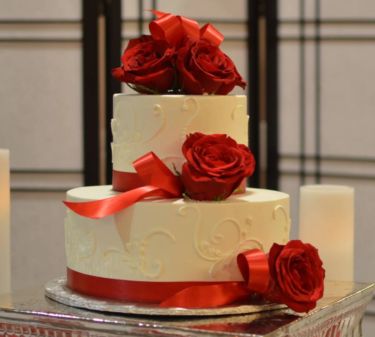 Two-tier wedding cake with red roses and satin ribbon cascading down the tiers