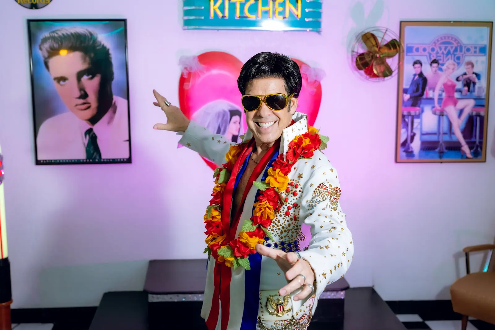 Elvis impersonator in a white jumpsuit and lei poses in a retro diner room at Viva Las Vegas Weddings