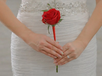 A single long-stemmed red rose held gently by the bride