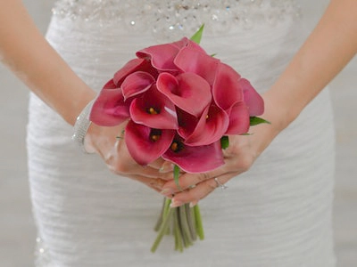 Pink calla lily bouquet wrapped with greenery held by bride