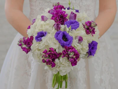 Bride holds a white hydrangea bouquet with purple and pink flowers