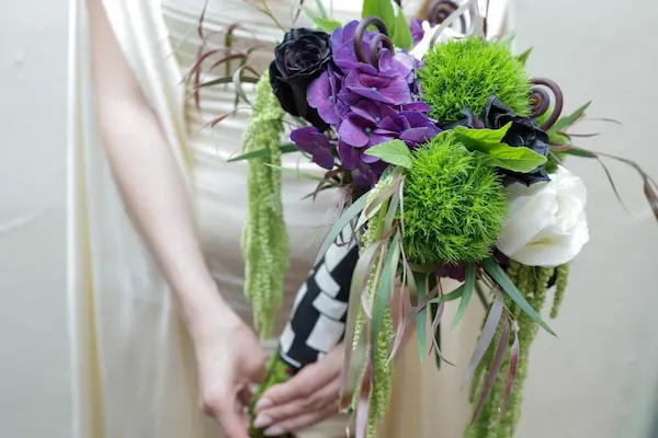 Bride holds a Beetlejuice-themed bouquet with purple hydrangeas and green accents