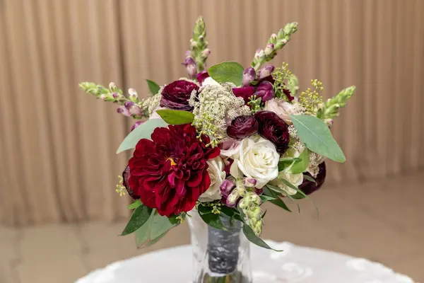 Rich burgundy and cream bouquet with dahlias, ranunculus, and snapdragons displayed in a vase