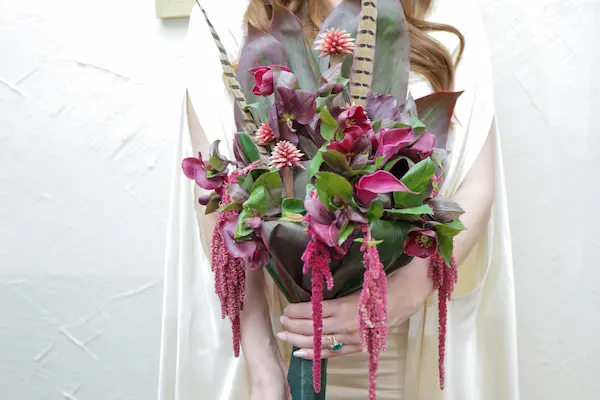 Bride holds a dramatic burgundy bouquet with feathers and cascading amaranthus