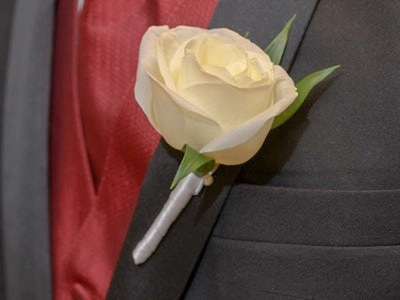 White rose boutonniere pinned to a gray suit jacket with a red tie