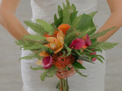 Bride holds a tropical bouquet with orange orchids and pink calla lilies