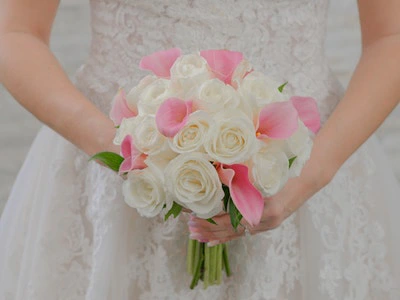 A soft bouquet of white roses and pink calla lilies held by the bride