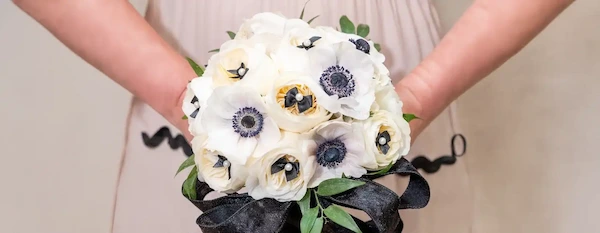 Bride holds a white anemone bouquet tied with a black ribbon