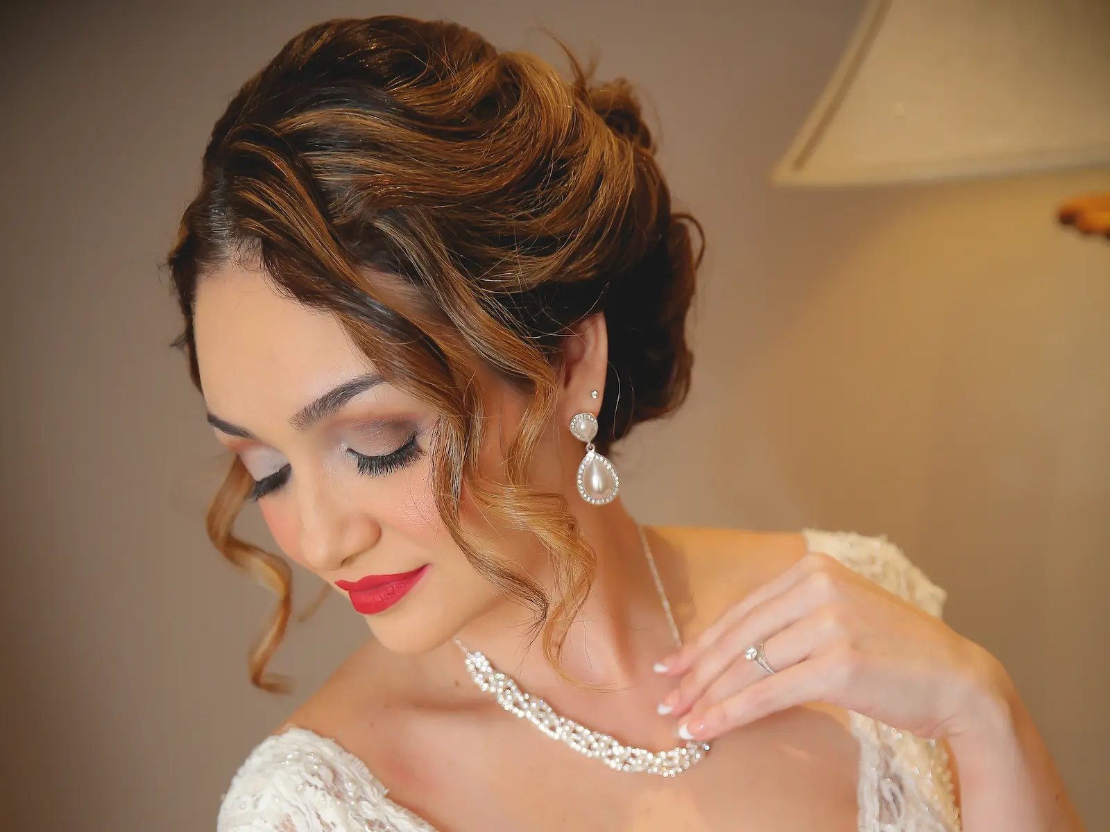 Bride with red lips, smoky eye airbrush makeup, pearl earrings, and curled updo for her wedding